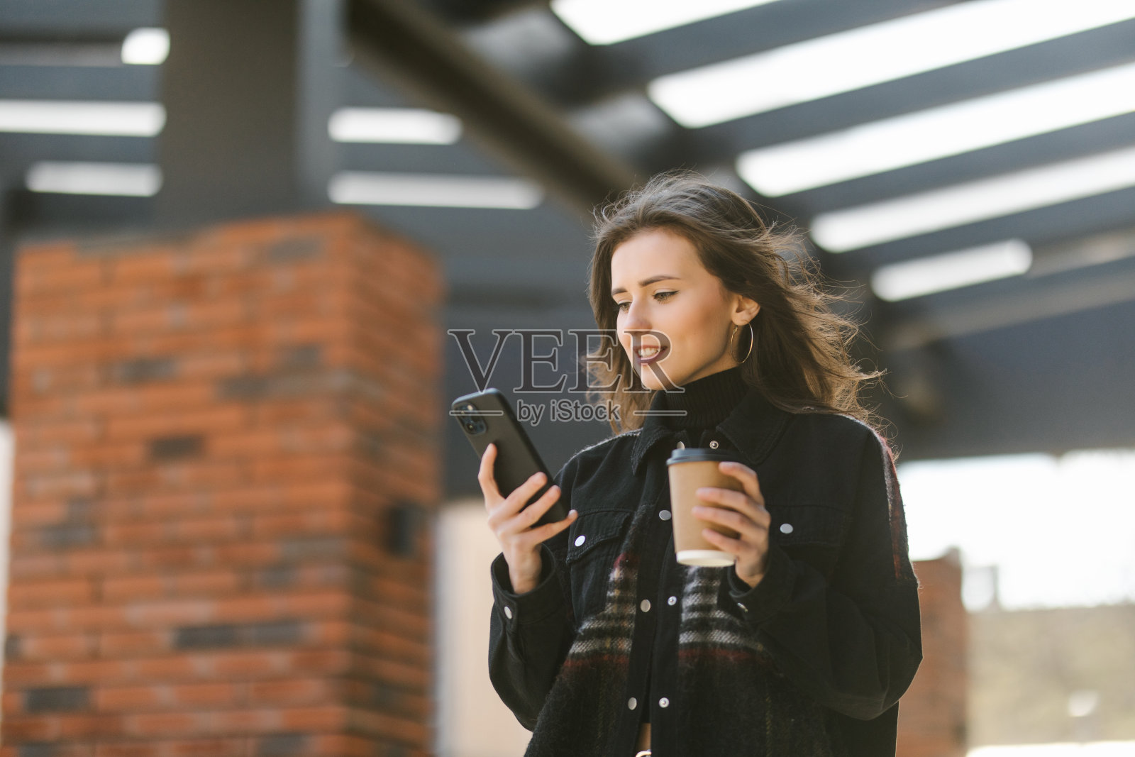 开朗的女人在街上喝着早茶，用着智能手机。照片摄影图片