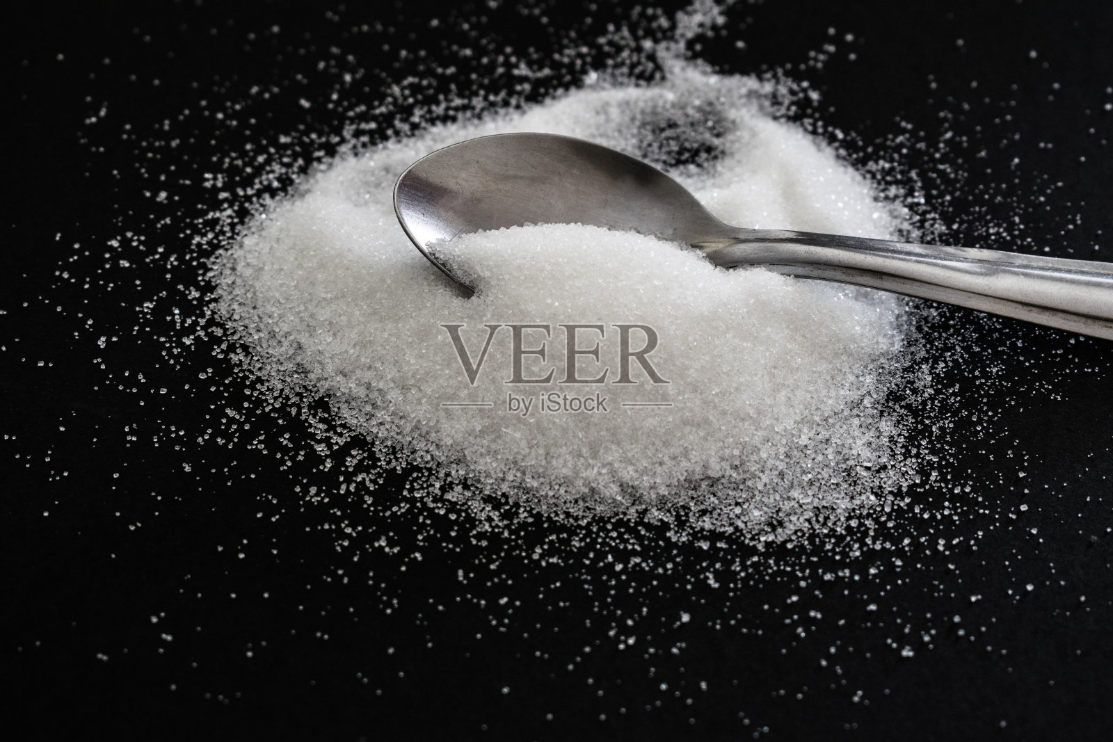 在黑色背景上用茶匙堆上糖照片摄影图片