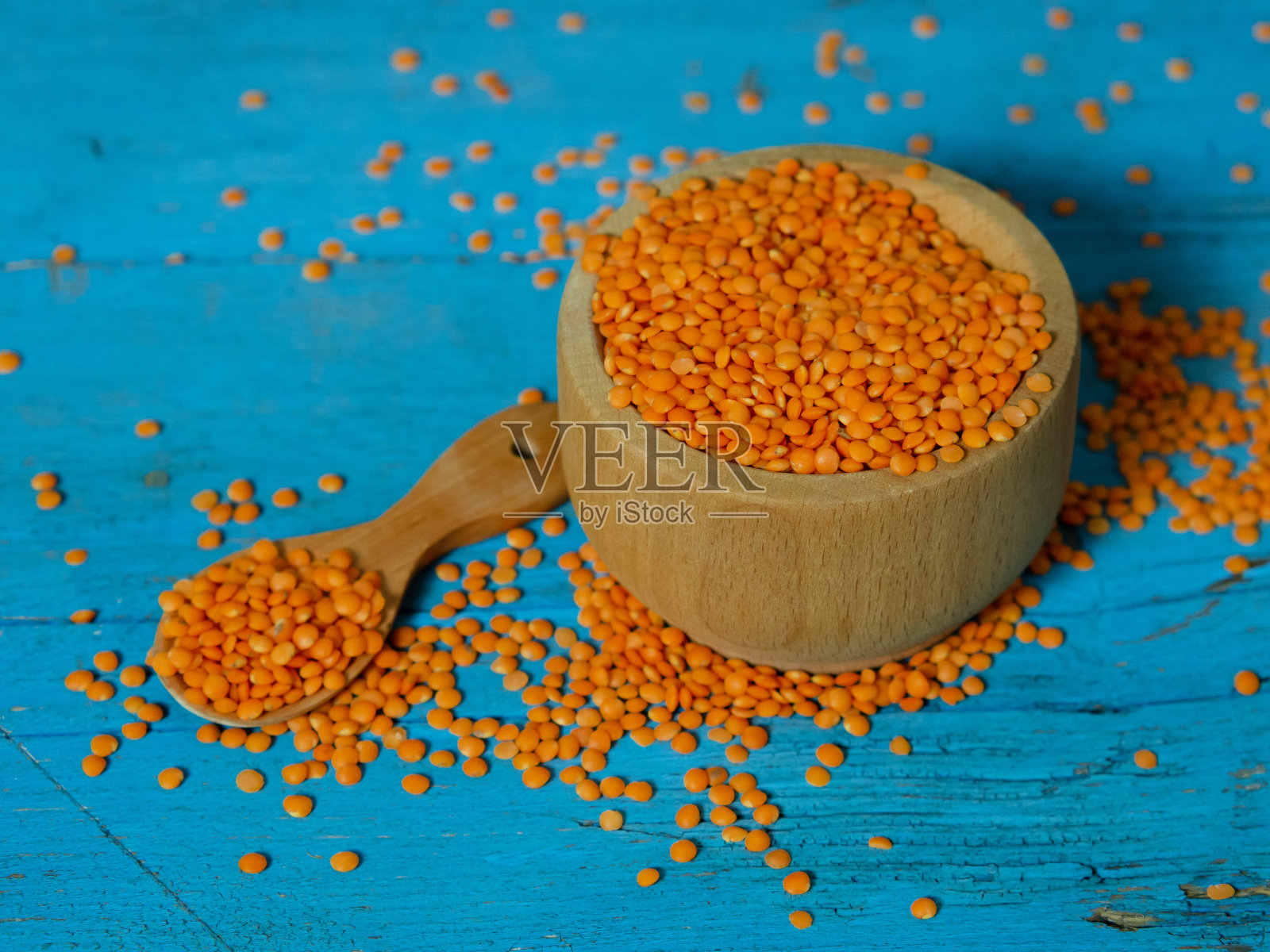 在一张古老的乡村桌子上，木盘和木勺里装着红扁豆。素食。照片摄影图片