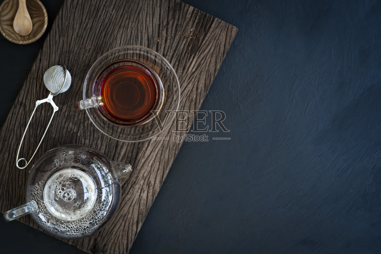 热茶装在一个玻璃茶壶和杯子装饰干茶叶在一个小木碗和小勺子在旧木板与黑暗的厨房桌面背景俯视图照片摄影图片