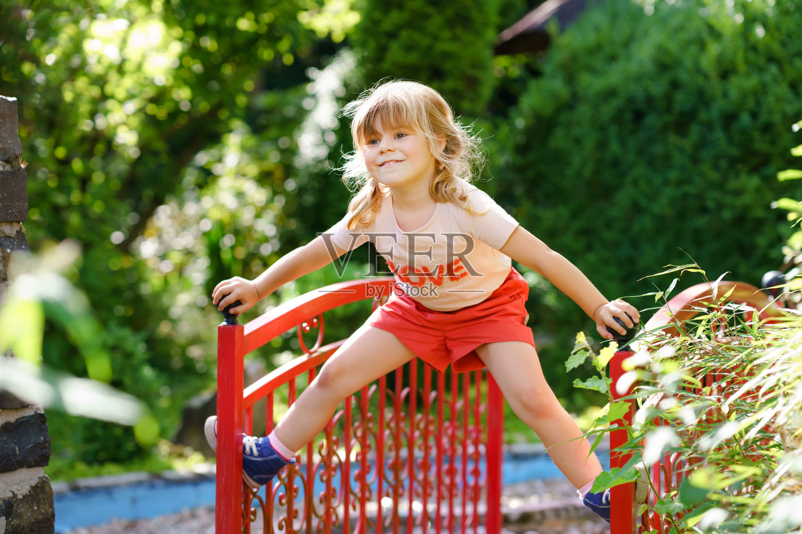 学前班的小女孩在户外操场上玩耍。快乐的幼儿攀爬和夏季户外活动的乐趣。照片摄影图片