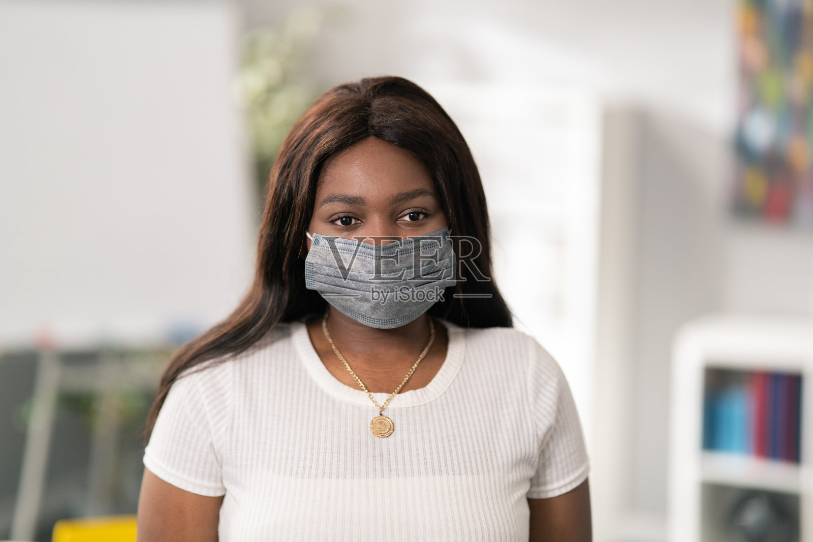 年轻漂亮的女孩的肖像长发，黑眼睛和皮肤，白色的t恤，奖章，项链脖子上，她有面具的脸，模糊的背景，学校教室，学生照片摄影图片