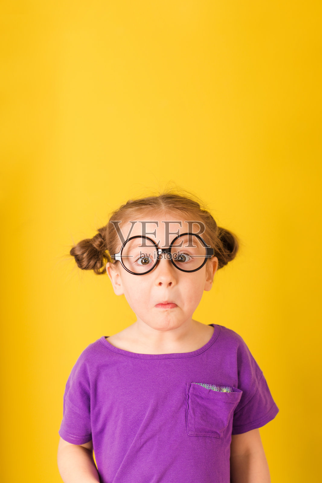 小可爱的白人有趣的惊讶，小女孩，戴着眼镜，紫色t恤，黄色的墙背景。儿童工作室肖像。照片摄影图片