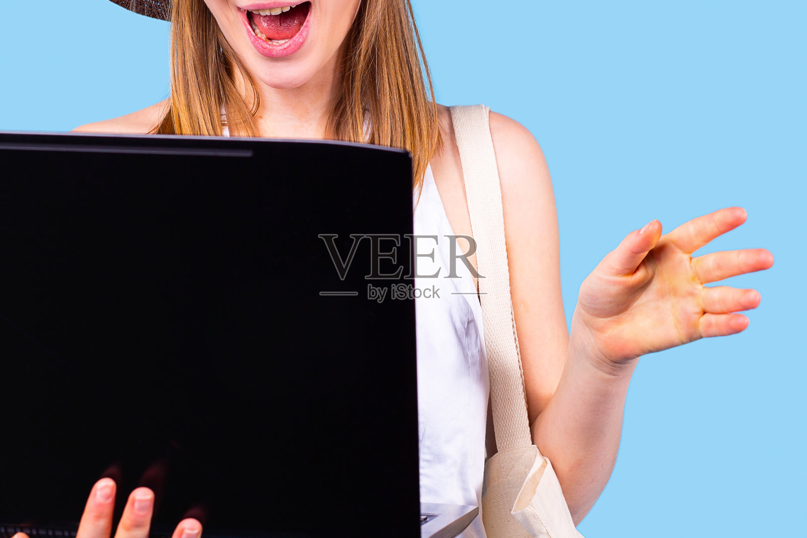 惊讶的美丽的年轻金发女人拿着笔记本电脑打开，拿着她的手到侧手掌向前。照片摄影图片