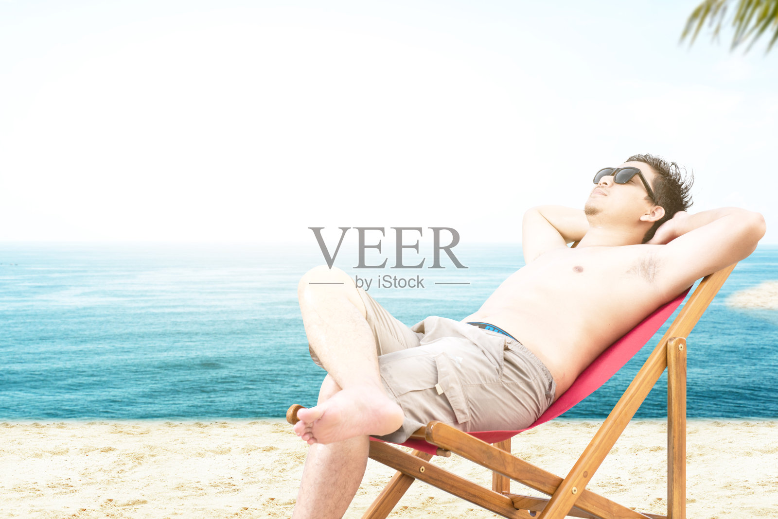 亚洲男人戴着太阳镜，坐在沙滩椅上休息照片摄影图片