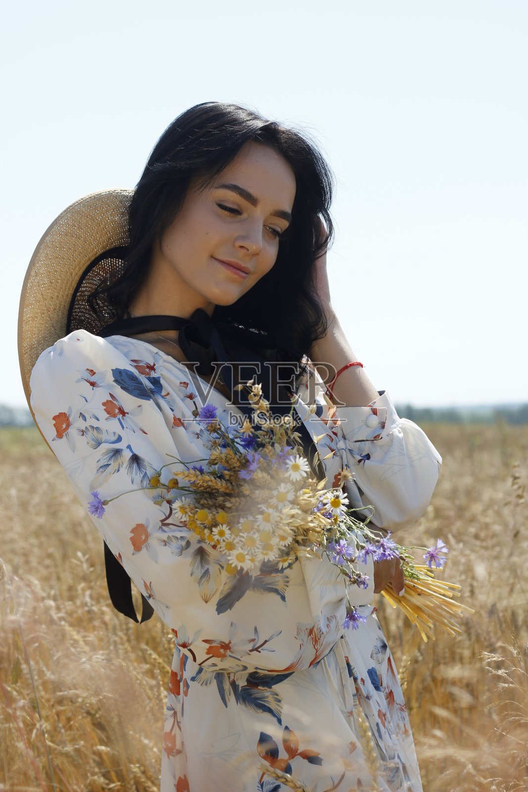 快乐的年轻黑发女孩草帽手持野花花束享受生活。美丽的大自然。自由的概念。明媚阳光下的乡村风景。麦穗背景。照片摄影图片