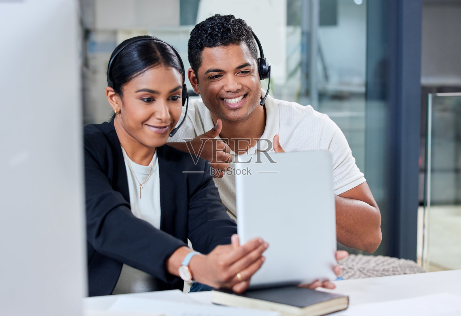 两名年轻的商务人士坐在一起，戴着耳机，用电子平板电脑自拍照片摄影图片