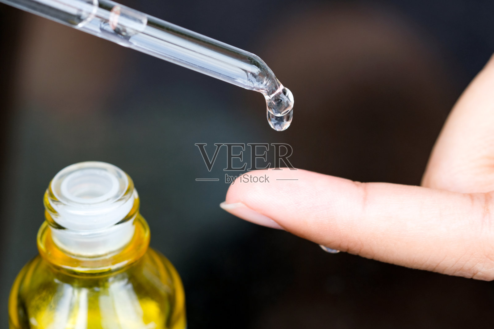 将面部血清胶原蛋白润肤霜滴入淡黄色瓶底。护肤精华油、维他命c、美容spa概念照片摄影图片