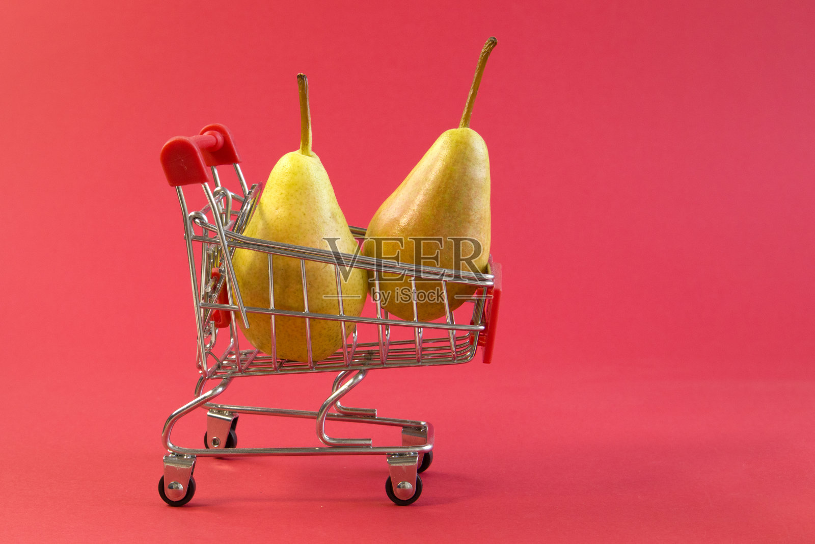 近距离观察小购物车与鲜嫩多汁的黄色梨在明亮的红色背景照片摄影图片