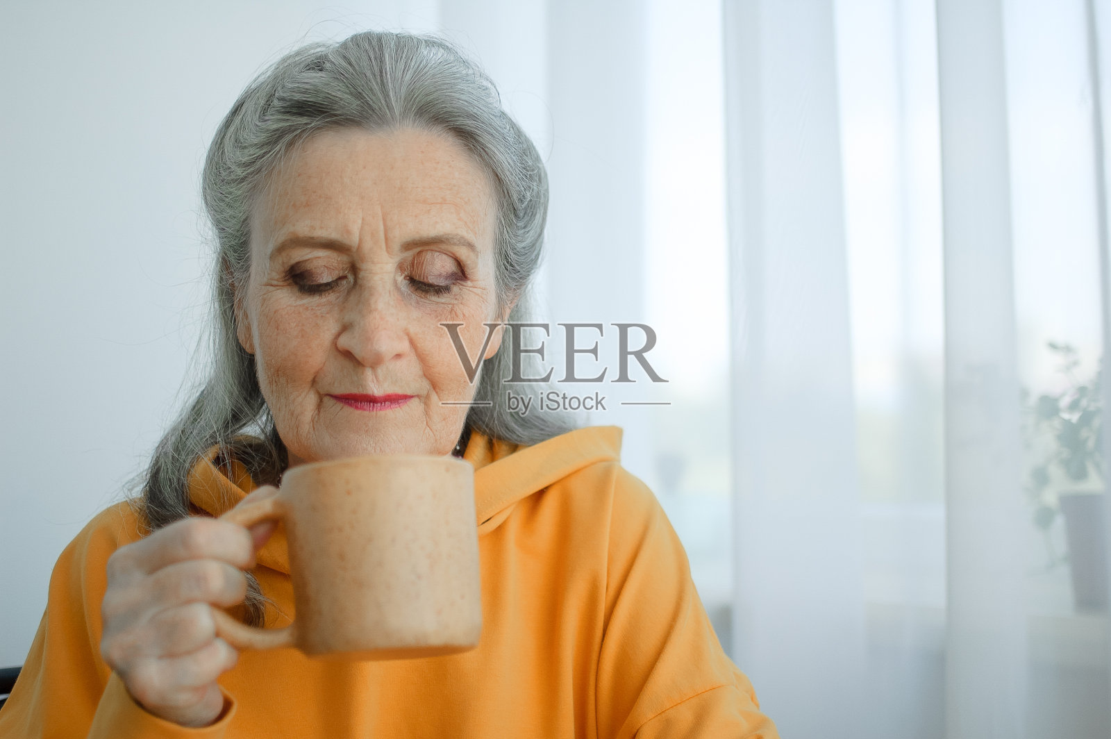 快乐的退休老人，古怪的灰发黄衣女人正在喝茶，若有所思地看着一个杯子照片摄影图片