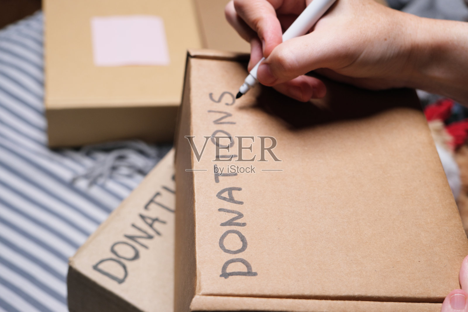 一位妇女坐在床上，在准备捐赠的箱子上签名照片摄影图片