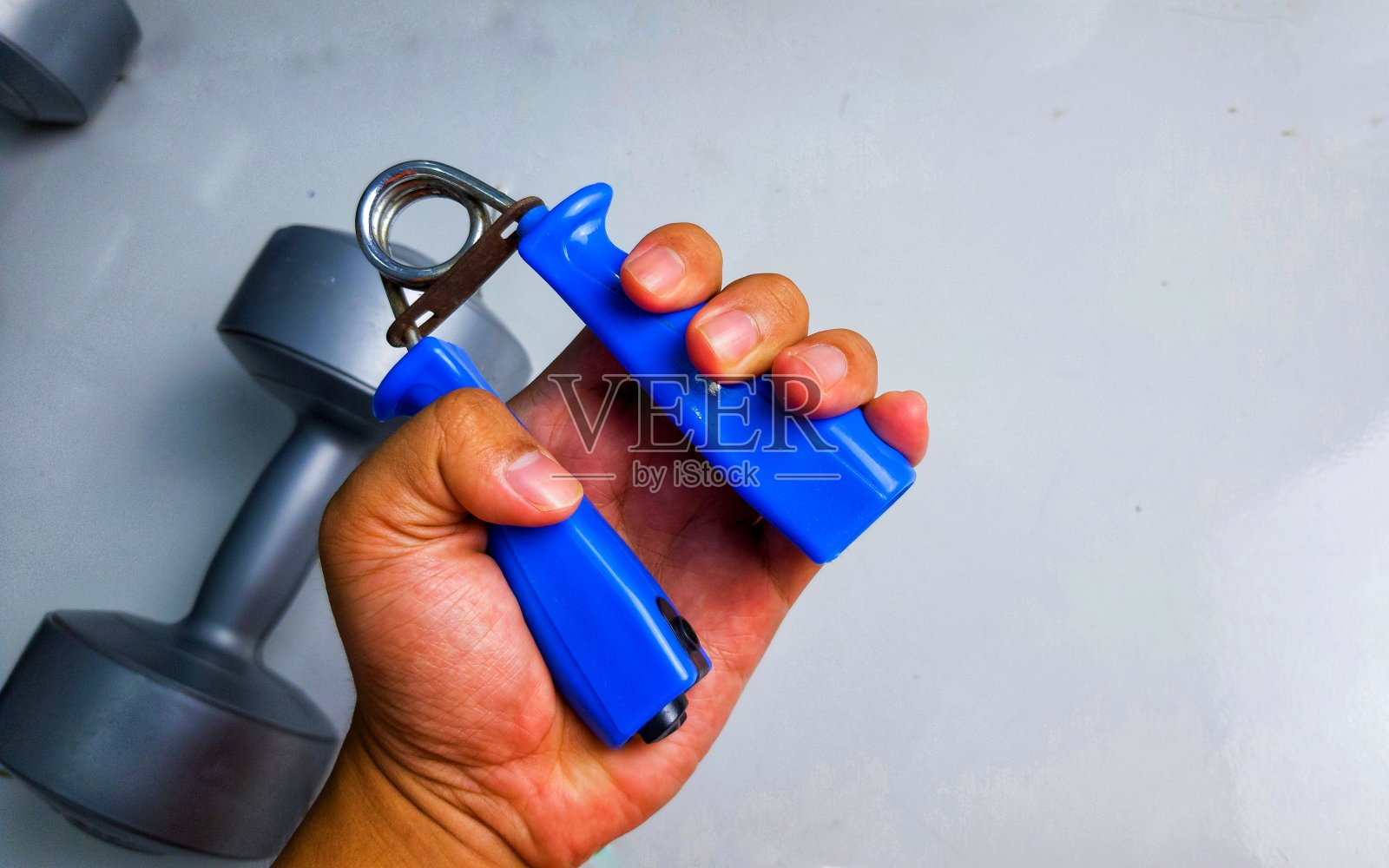东南亚男人的手，蓝色的手扩张器，白色背景上的抓手器和哑铃。手握加强工具照片摄影图片