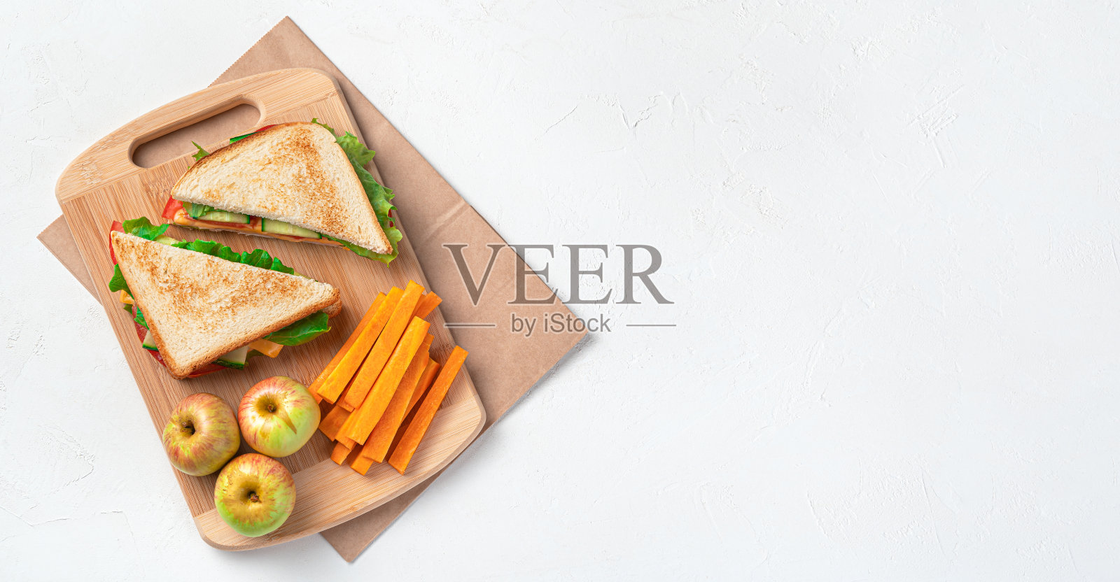 三明治，苹果和胡萝卜放在灰色背景的牛皮纸袋子上。准备学校午餐照片摄影图片