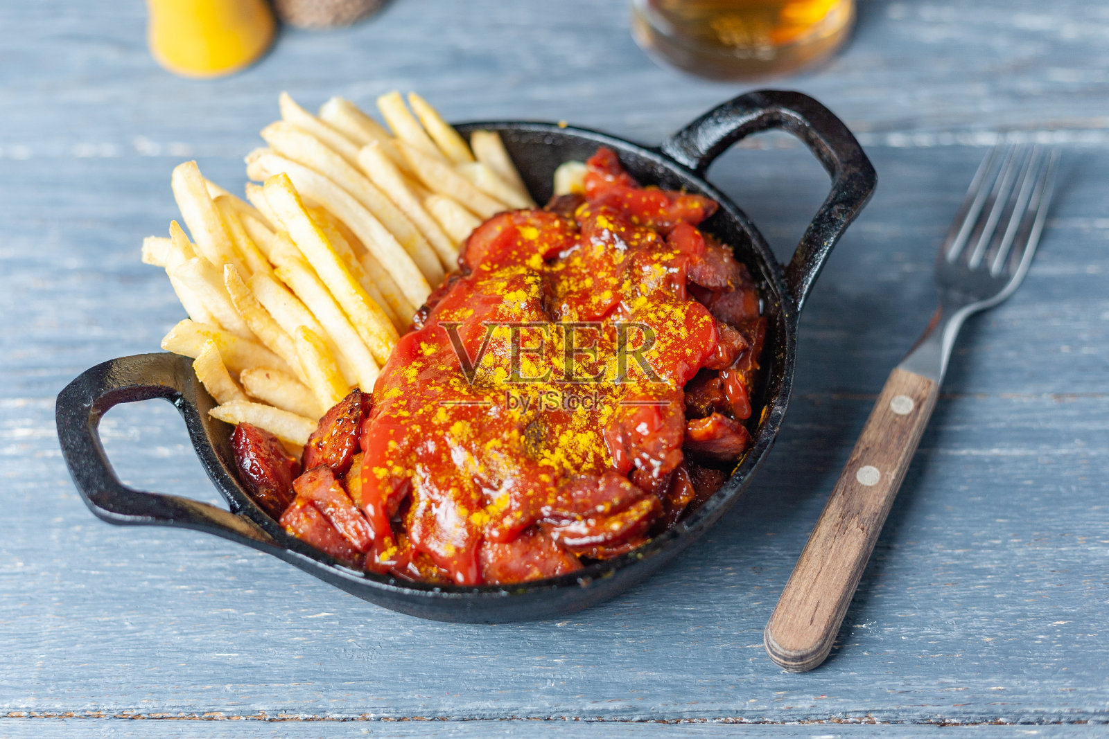 木桌上的黑色平底锅里放着咖喱香肠和炸薯条。照片摄影图片