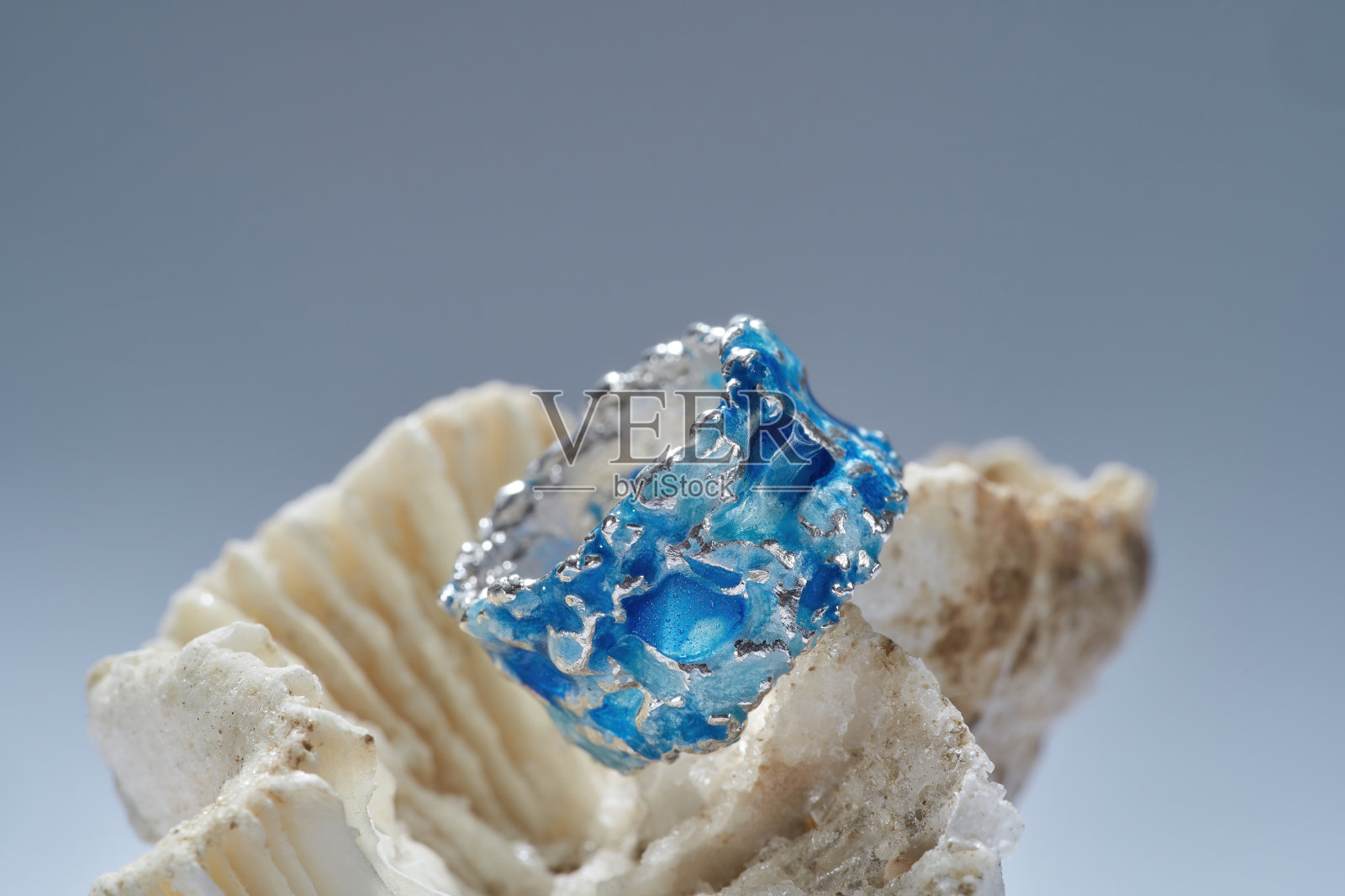 近距离拍摄的时尚戒指由银与蓝色珐琅在顶部安排在贝壳隔离在梯度背景照片摄影图片