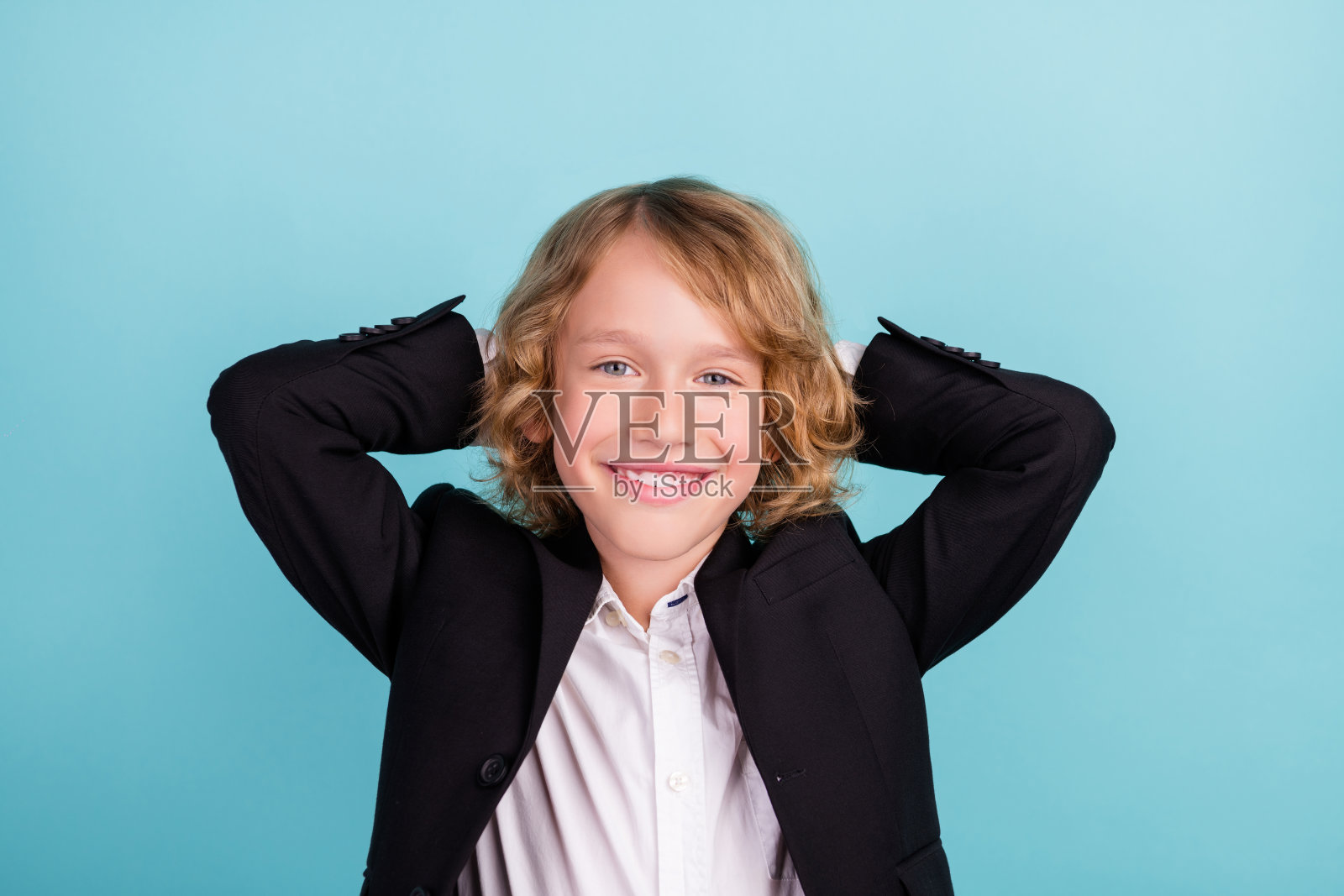 照片中可爱的金发小男孩双手头穿制服，孤立在蓝色背景上照片摄影图片