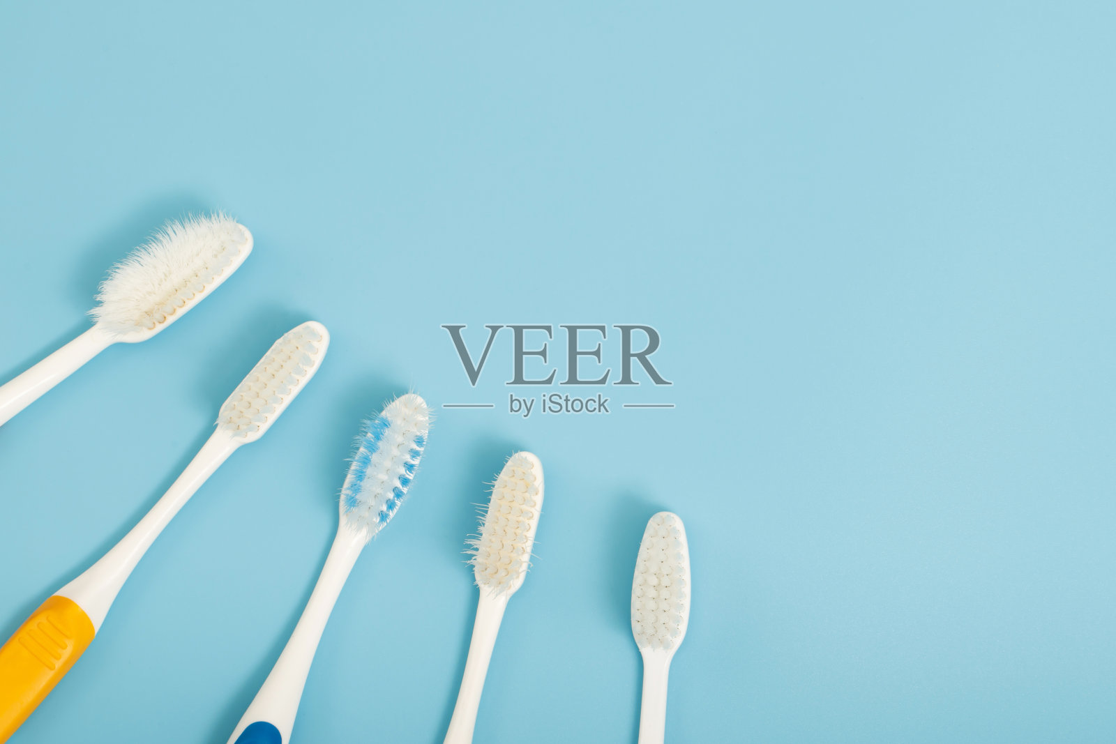 旧牙刷在蓝色背景上使用了过期(损坏)的各种颜色。专业牙医或经常更换牙刷。照片摄影图片