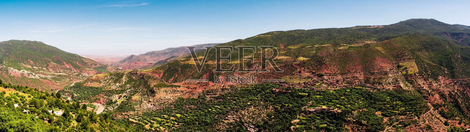 红摩洛哥阿特拉斯山脉，覆盖着绿树和植物。背景是蓝色无云的天空。照片摄影图片