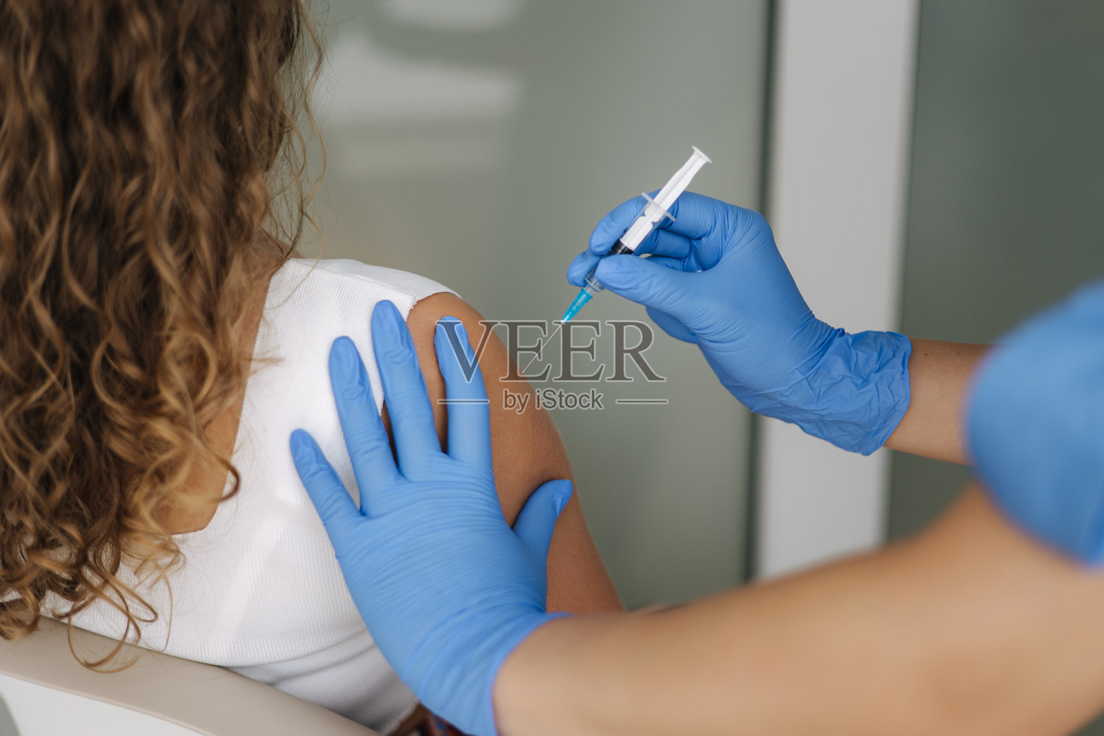女医生戴着防护手套，拿着注射器接种新冠疫苗。女性接受肩部注射。疫苗临床试验概念，冠状病毒照片摄影图片