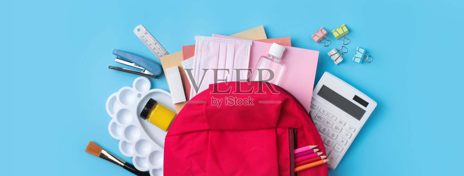 粉红色背包与文具在蓝色的桌子背景。照片摄影图片