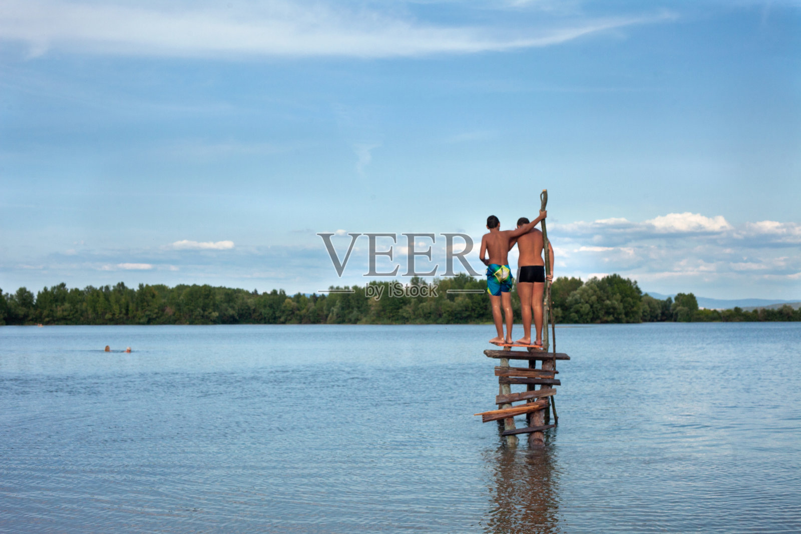 在一个美丽的湖上，两个男孩在一个旧的木制跳水板上照片摄影图片