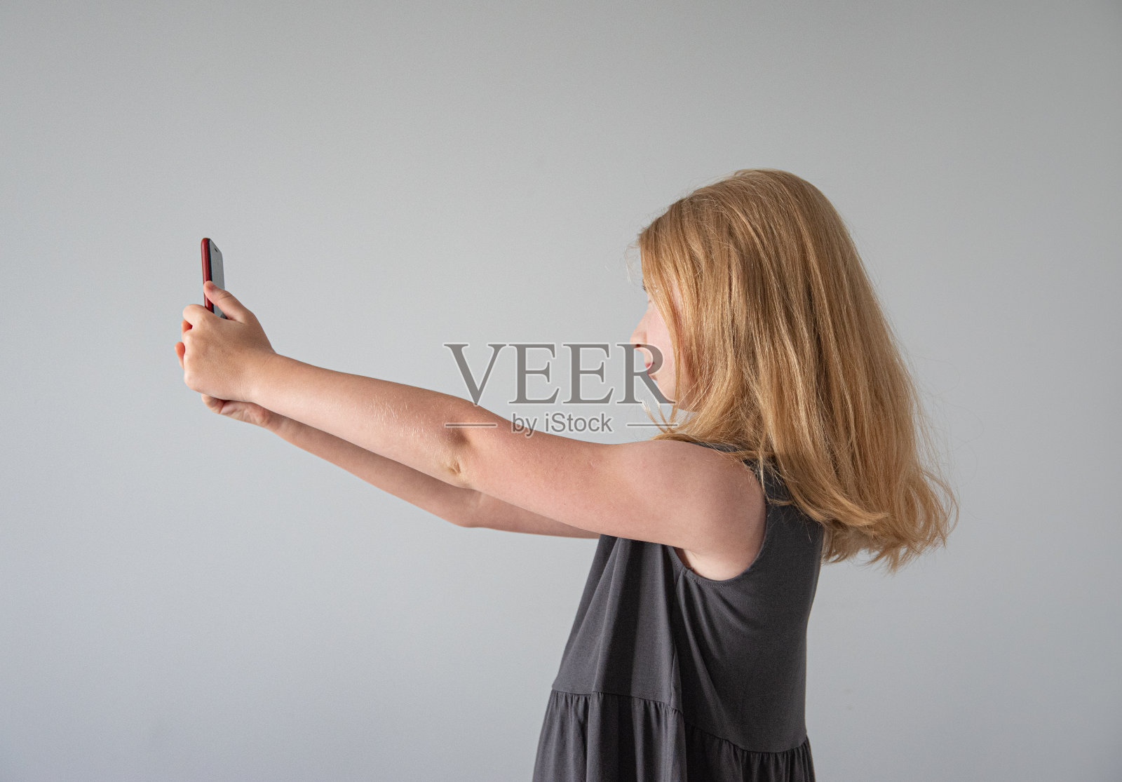 一个穿着灰色裙子，拿着手机在灰色背景下自拍的女孩照片摄影图片