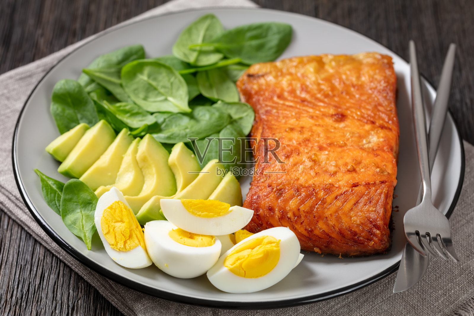 烤箱烤鲑鱼片与奶油熟透的鳄梨，嫩菠菜和水煮蛋放在沼泽橡木桌上的盘子上，从上面的水平视角，特写照片摄影图片