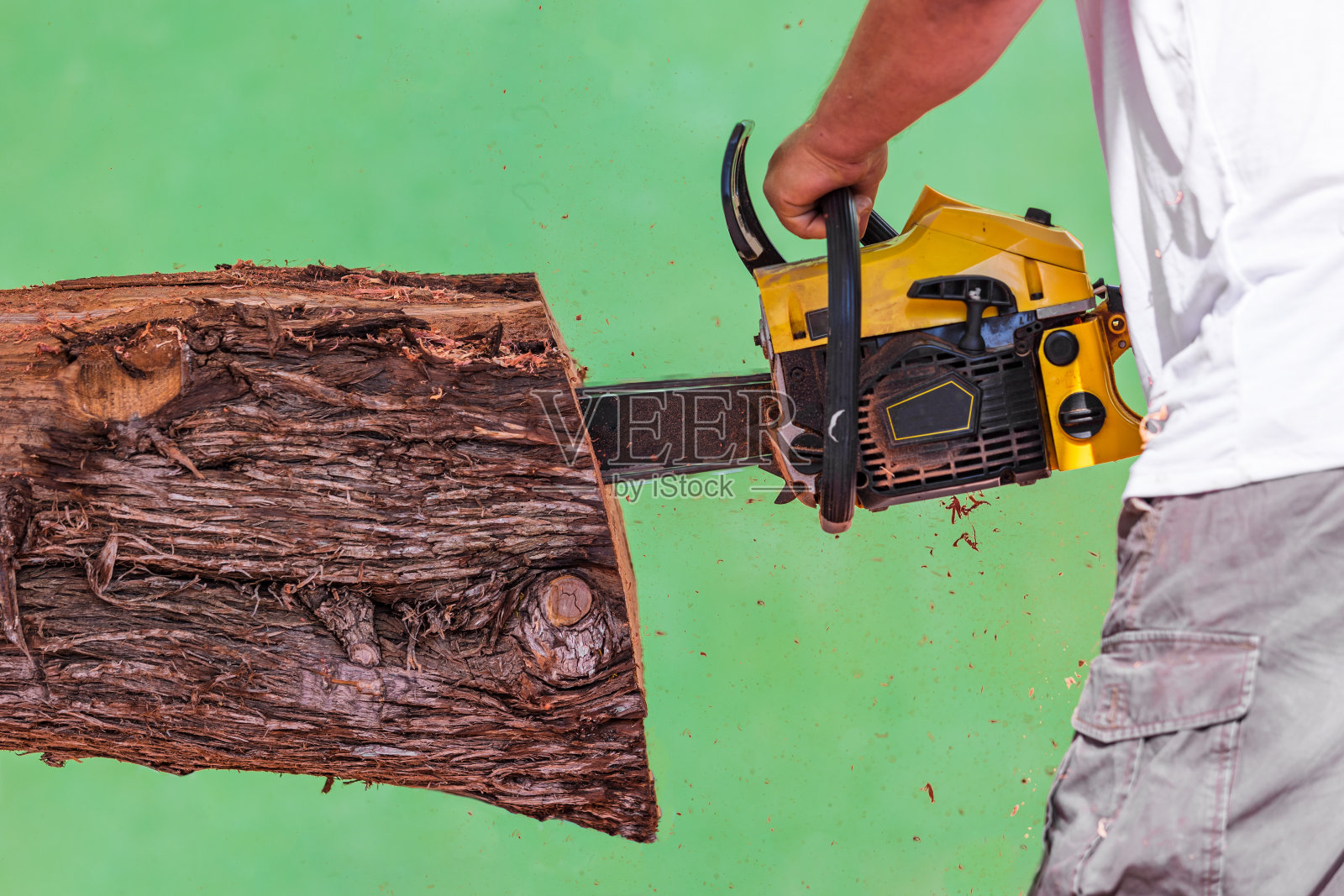 在绿色背景下，没有手套或安全元件的人用链锯切割原木照片摄影图片