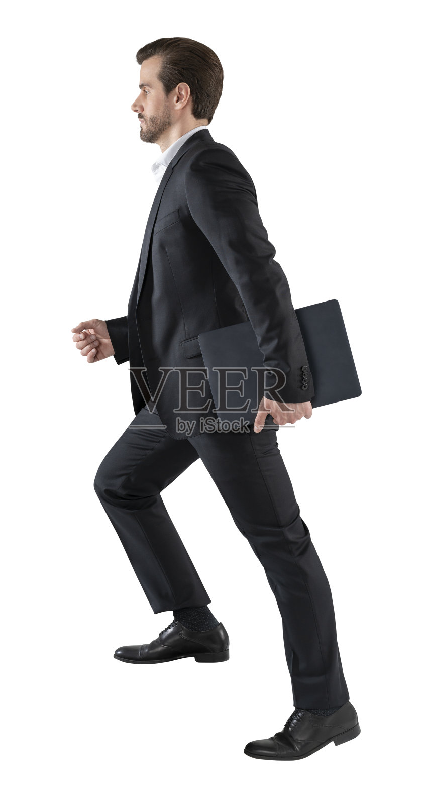 年轻的商人走着走着，商人穿着优雅的黑色西装，手里拿着笔记本电脑或文件夹。白色背景隔离照片摄影图片