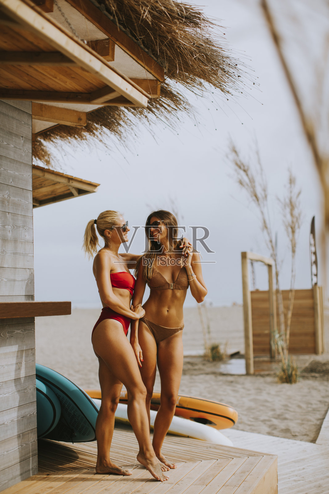 夏天，身穿比基尼的年轻女子站在海滩上的冲浪小屋旁照片摄影图片