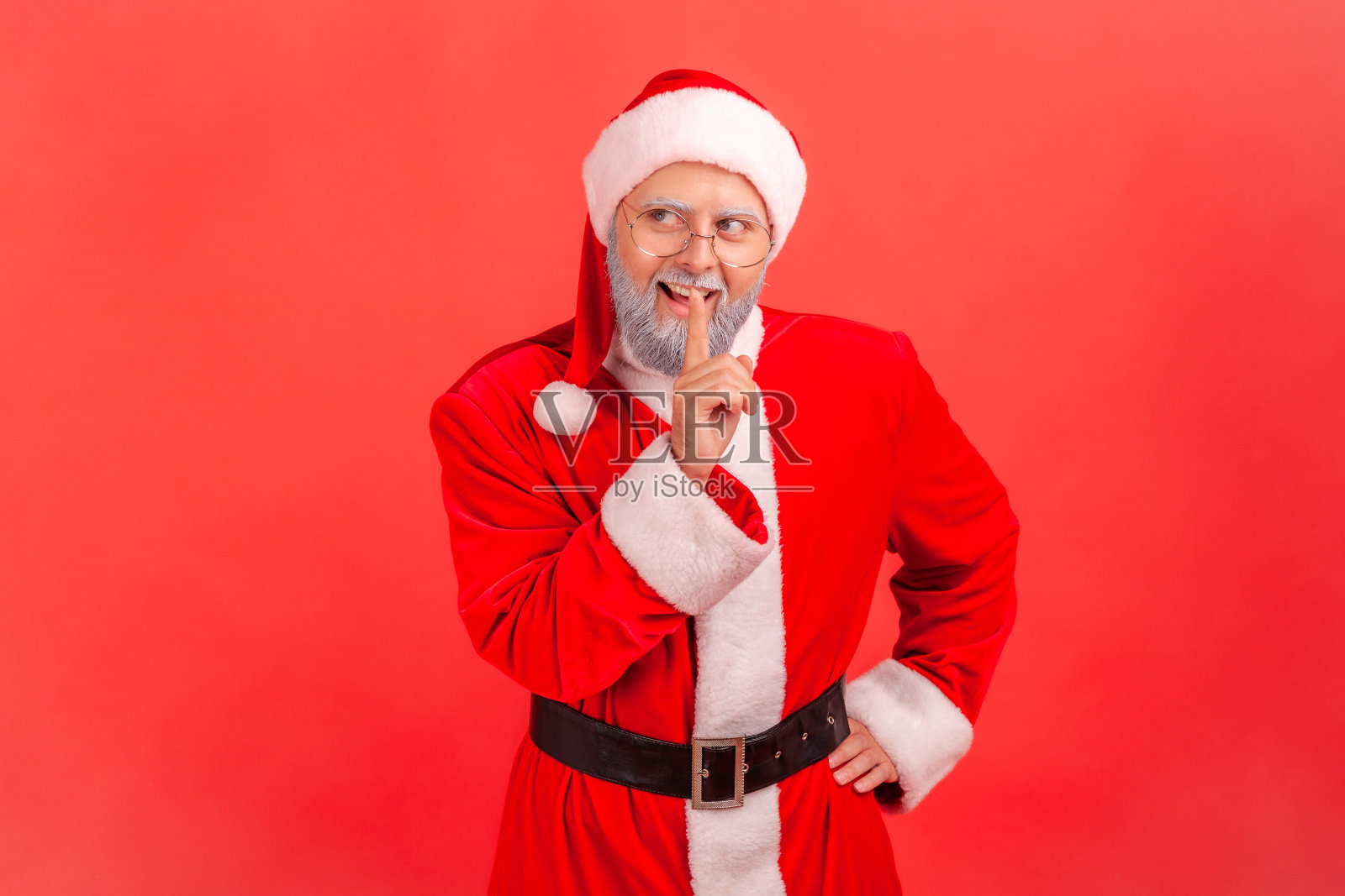 穿着圣诞老人服装、留着灰白胡子的老人沉默着，手指放在嘴唇上，对着镜头微笑，要求保守秘密。照片摄影图片