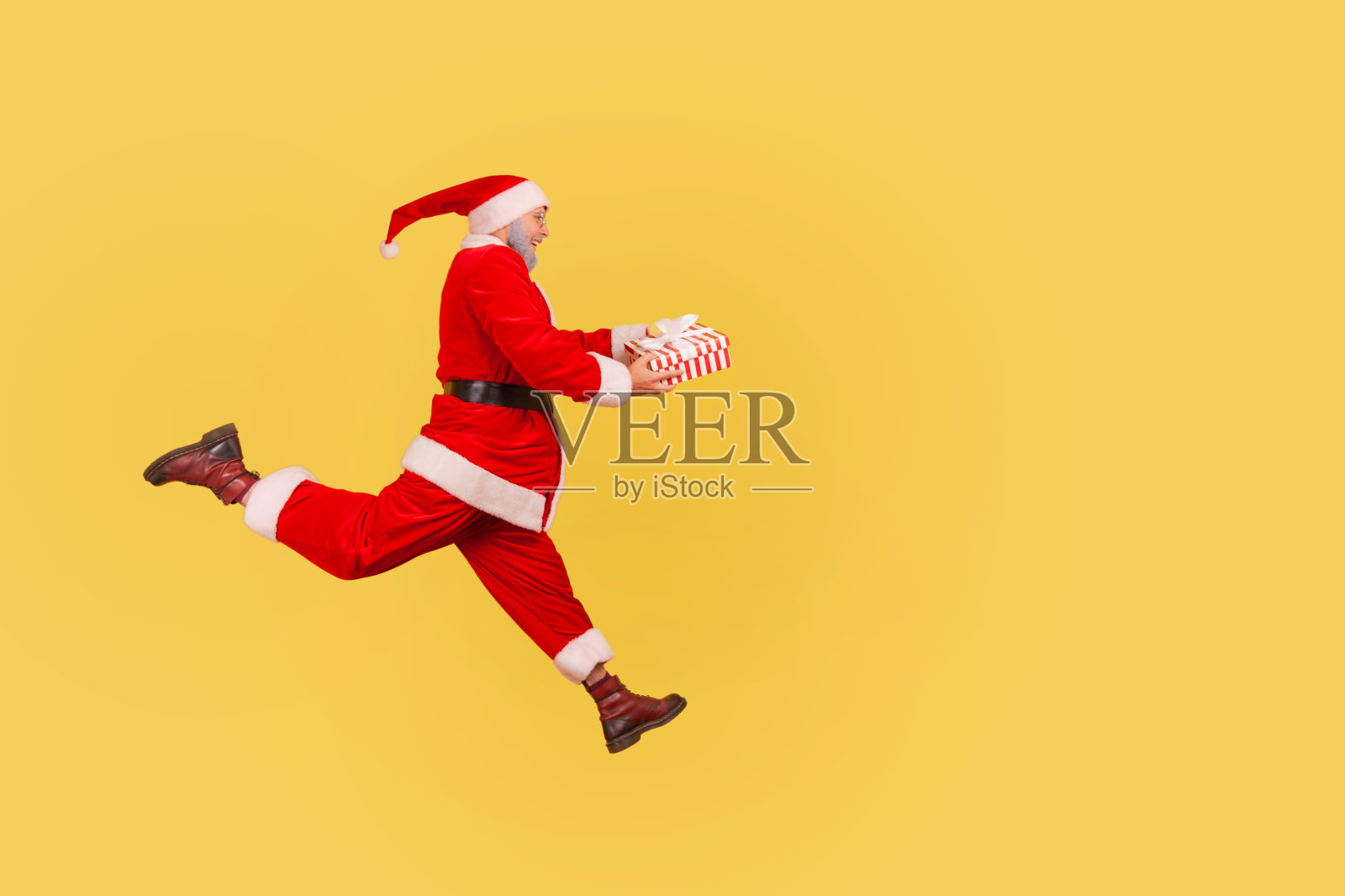 一旁看到满脸胡子的老人穿着圣诞老人的服装，手里拿着礼物盒，正忙着去拜年。照片摄影图片