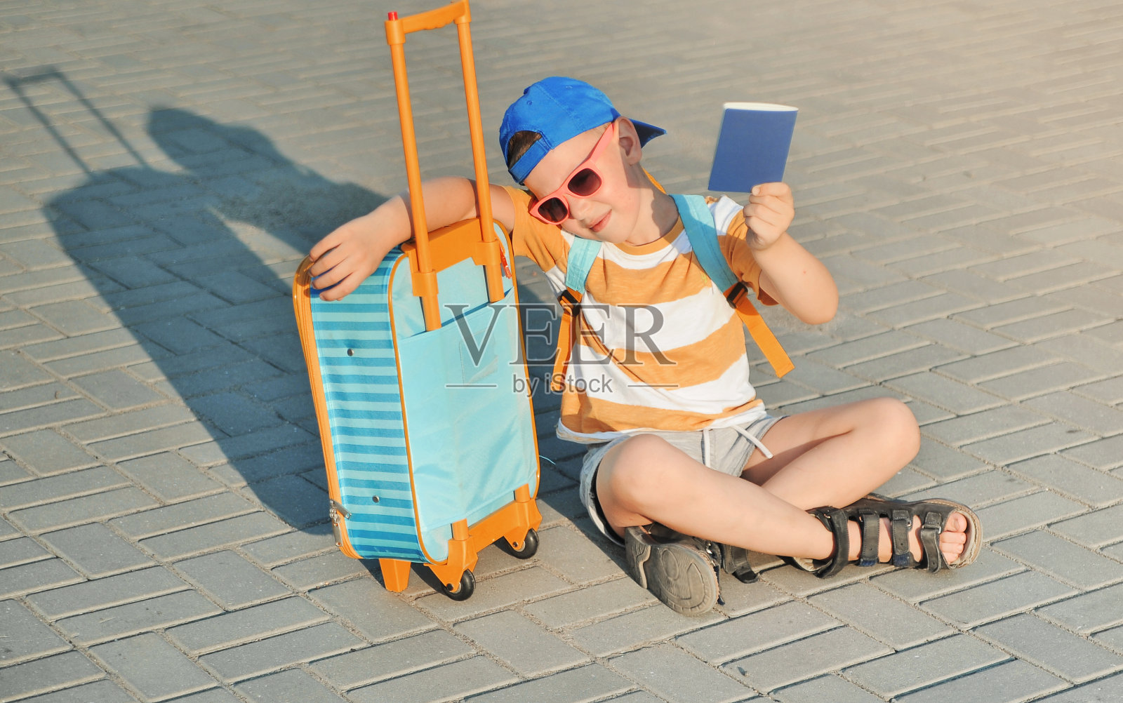 可爱的小男孩提着箱子走在路上。照片摄影图片