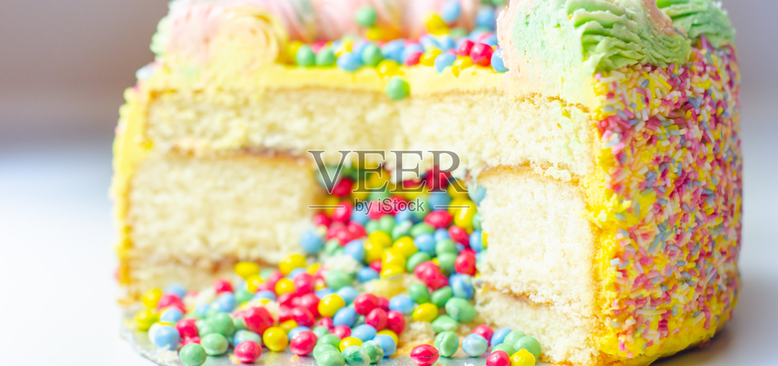 马德拉海绵蛋糕涂上黄色糖霜，分层李子和覆盆子果酱，填满和顶部的五彩巧克力尖，装饰着五彩糖霜和糖装饰照片摄影图片