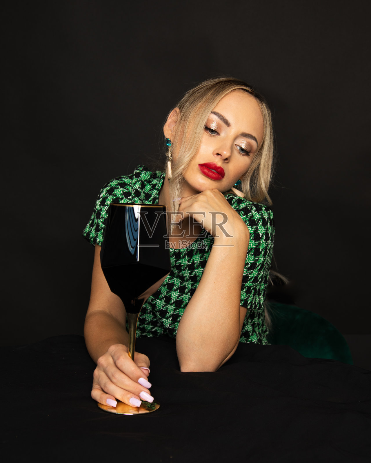 豪华的年轻金发女人在黑色背景的绿色衣服累了，厌倦了玻璃为酒精。上流社会的酗酒观念照片摄影图片