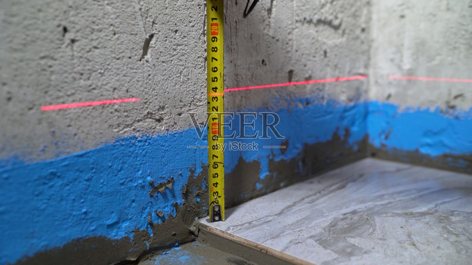 检查浴室里的瓷砖。瓷砖铺地时质量控制。铺瓷砖时，技术人员用尺子检查地板的水平度照片摄影图片