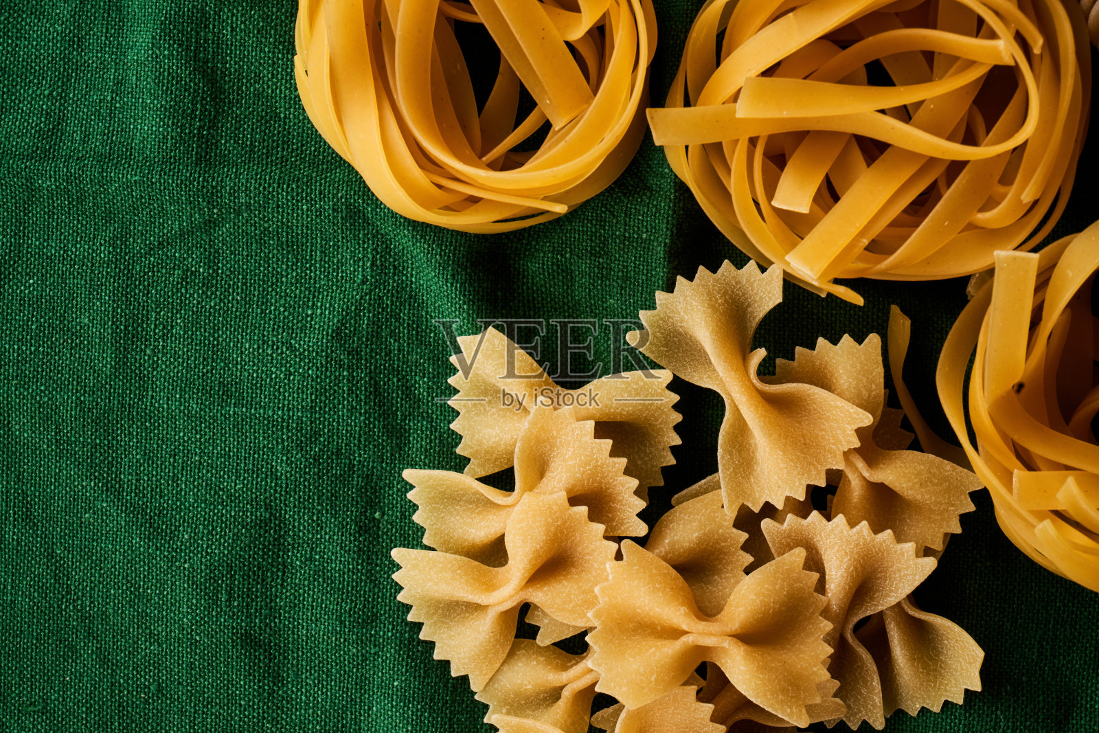 不同品种的面食混合在绿色面料的背景上，烹饪什锦通心粉的概念照片摄影图片