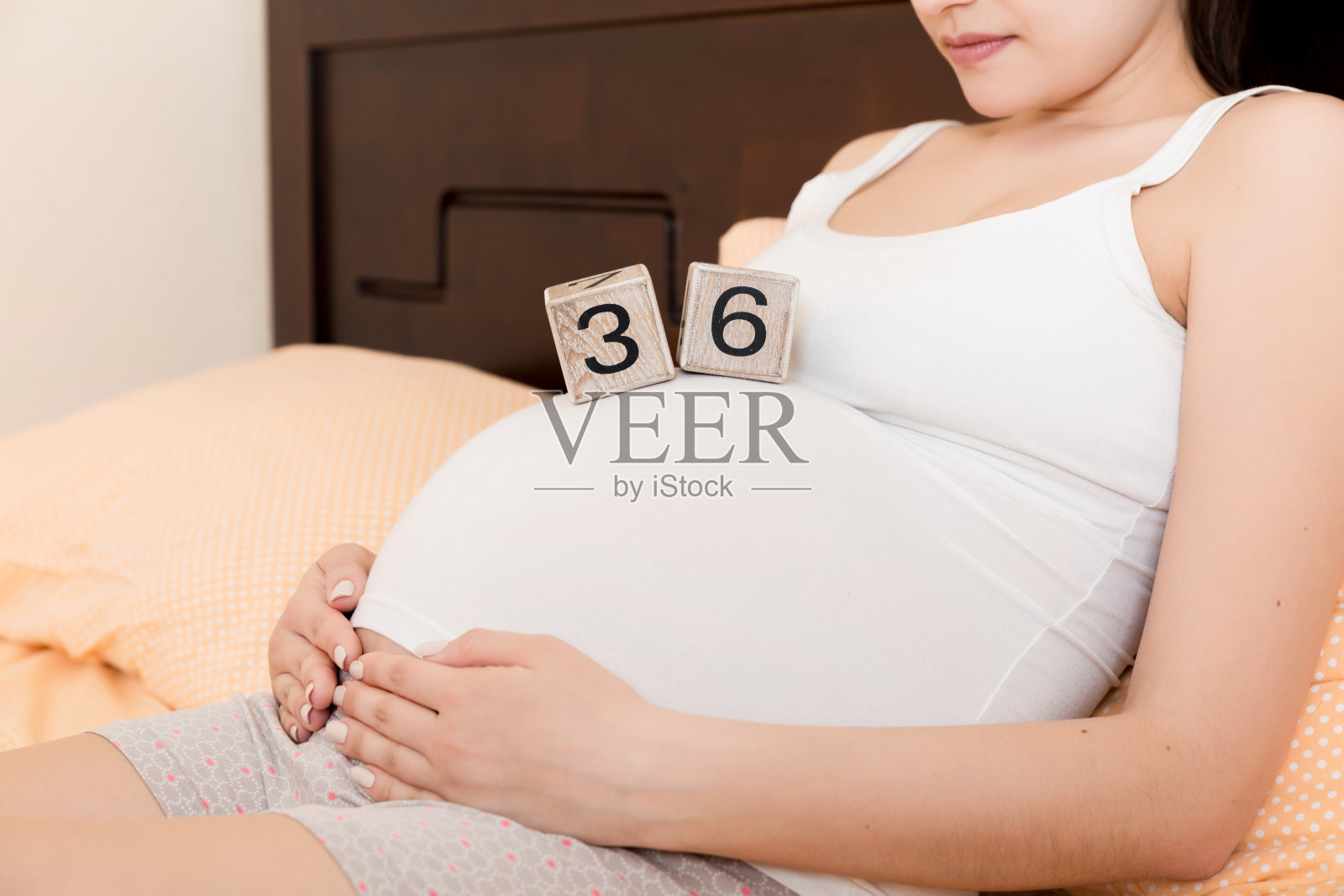 孕妇穿着白色内衣躺在家里的床上，手里拿着怀孕36周的日历。孕妇的概念。期待即将到来的孩子照片摄影图片