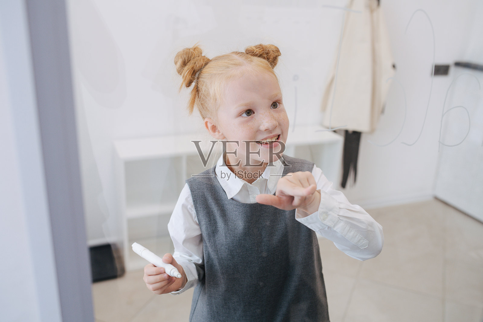 金发小女孩在白板上写字。正面的看法。照片摄影图片