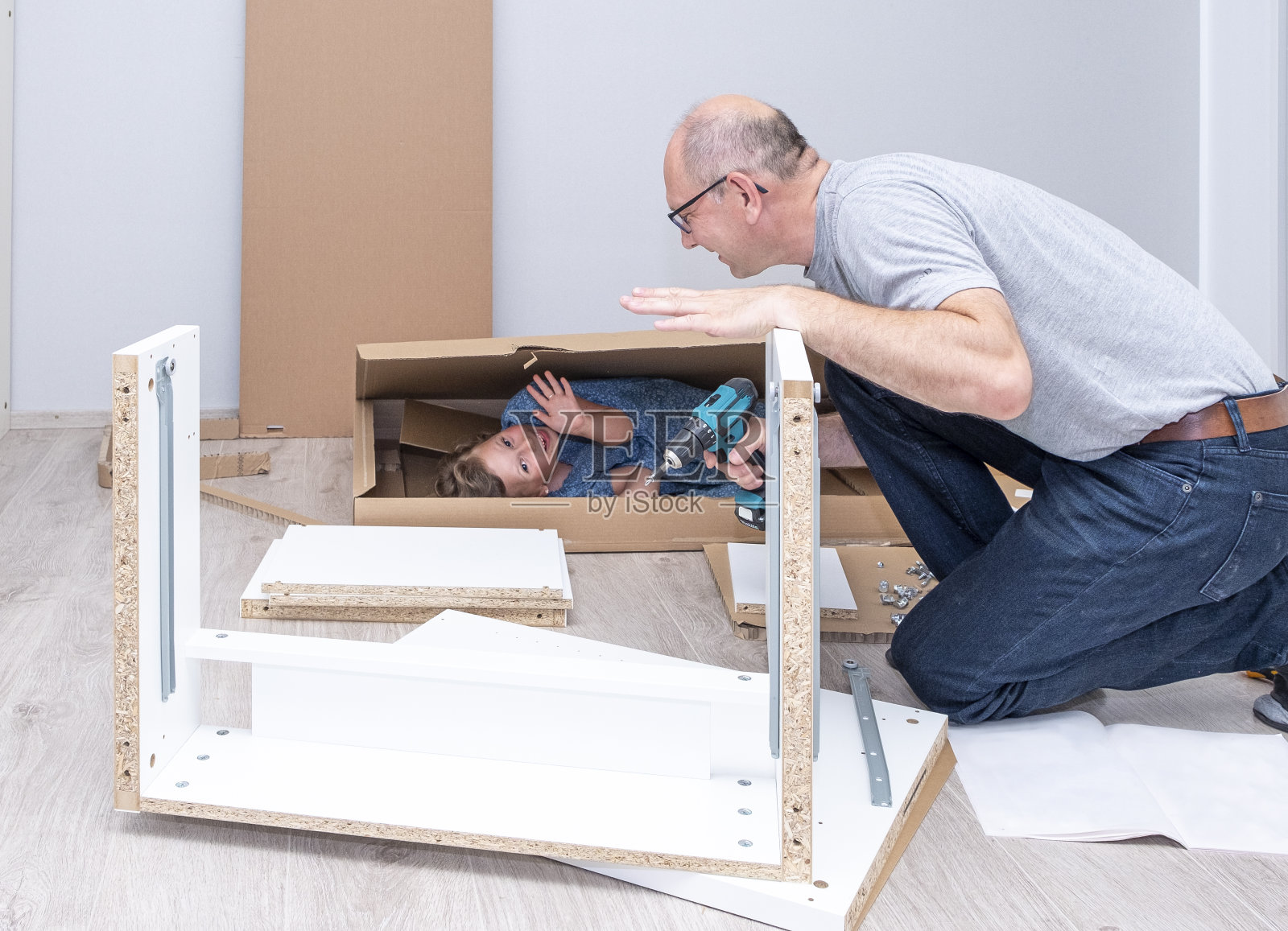 一个白人收集家具，一个小女孩藏在纸板箱里。照片摄影图片