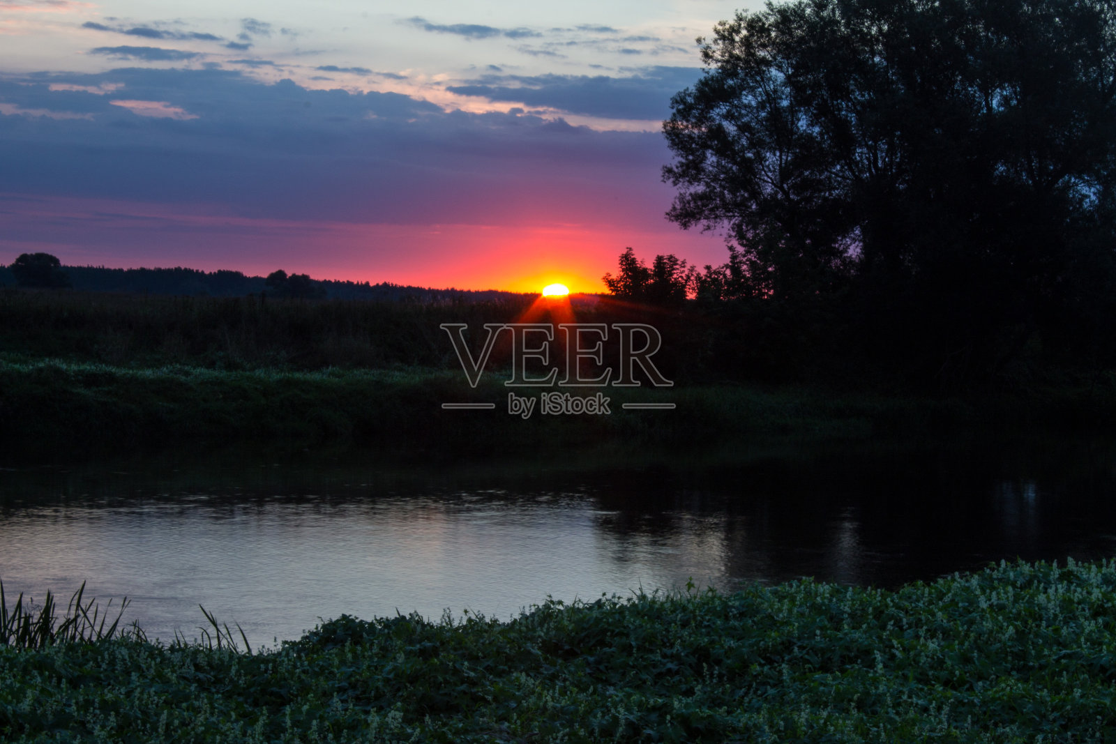 日出在河上，树木的轮廓在多云的天空背景下照片摄影图片