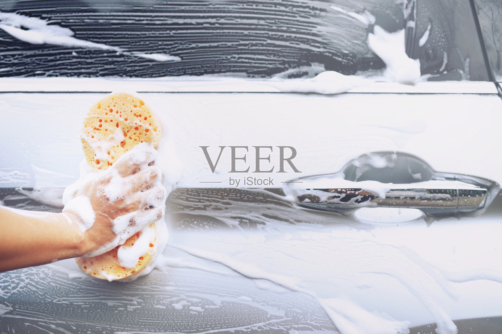 工人手拿黄色海绵和泡沫清洁剂清洗车窗。概念洗车清洁。留出书写信息的空间。照片摄影图片