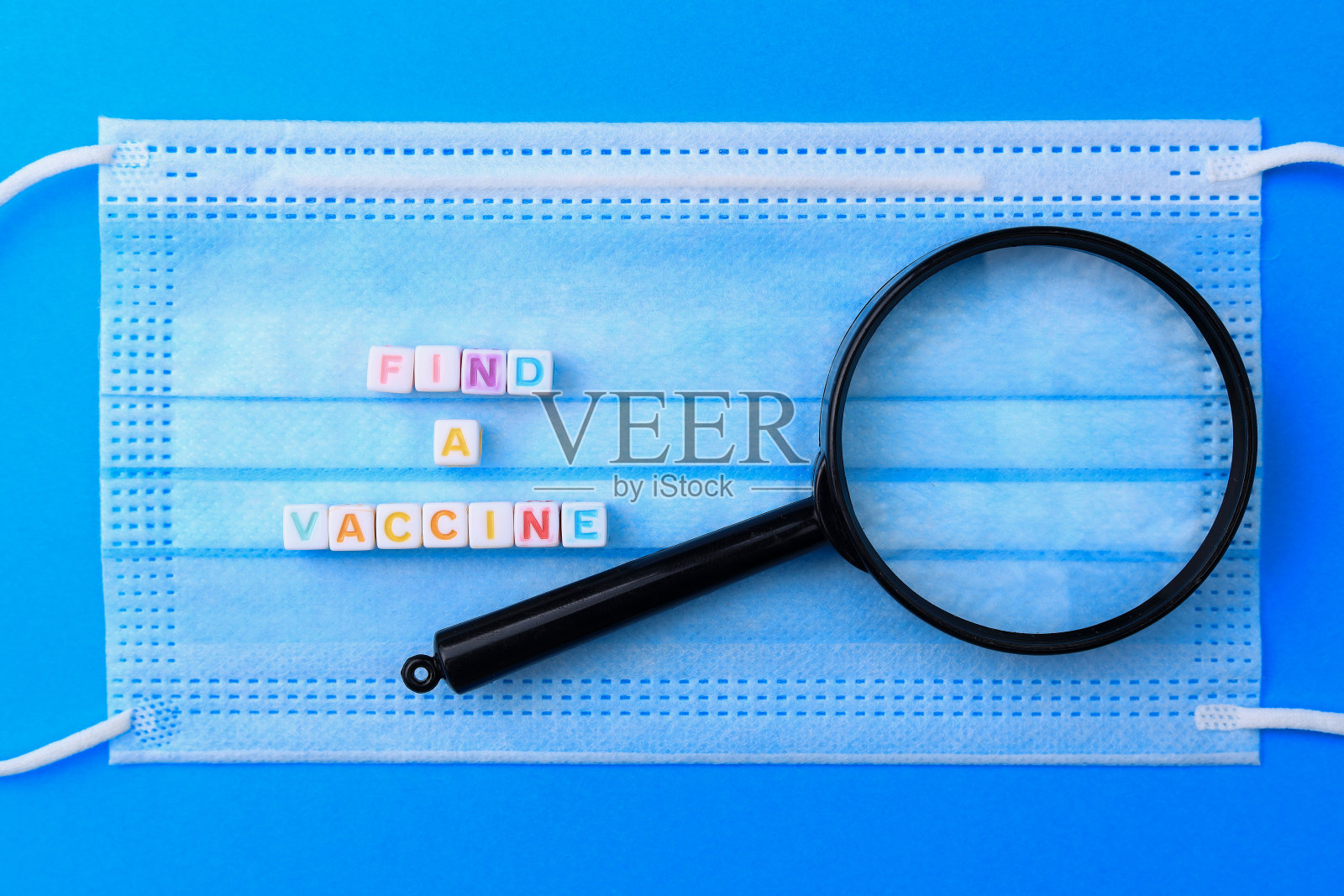 立方体形成文本找到疫苗用放大镜在医用外科口罩的背景上。照片摄影图片