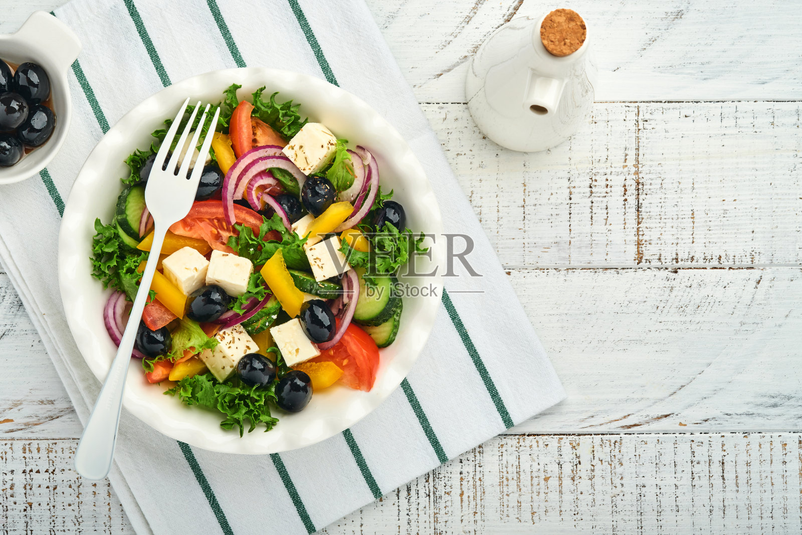 传统的希腊沙拉，新鲜的黄瓜，西红柿，甜椒，生菜，红洋葱，羊乳酪，橄榄和橄榄油放在白色盘子里。健康食品，俯视图。照片摄影图片