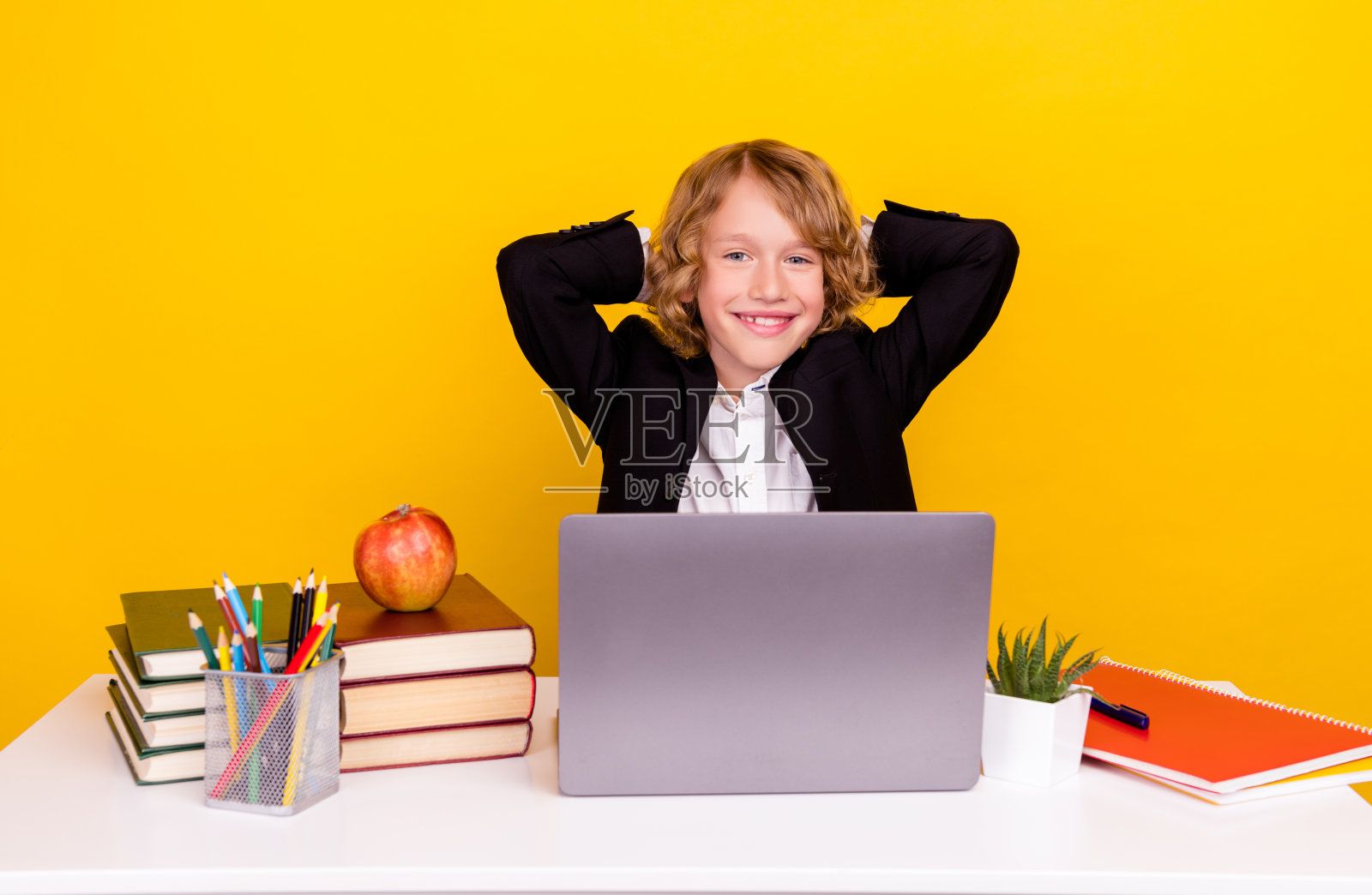 轻松的小学生坐在课桌上享受舒适的休息，穿着统一的隔离黄色背景照片摄影图片