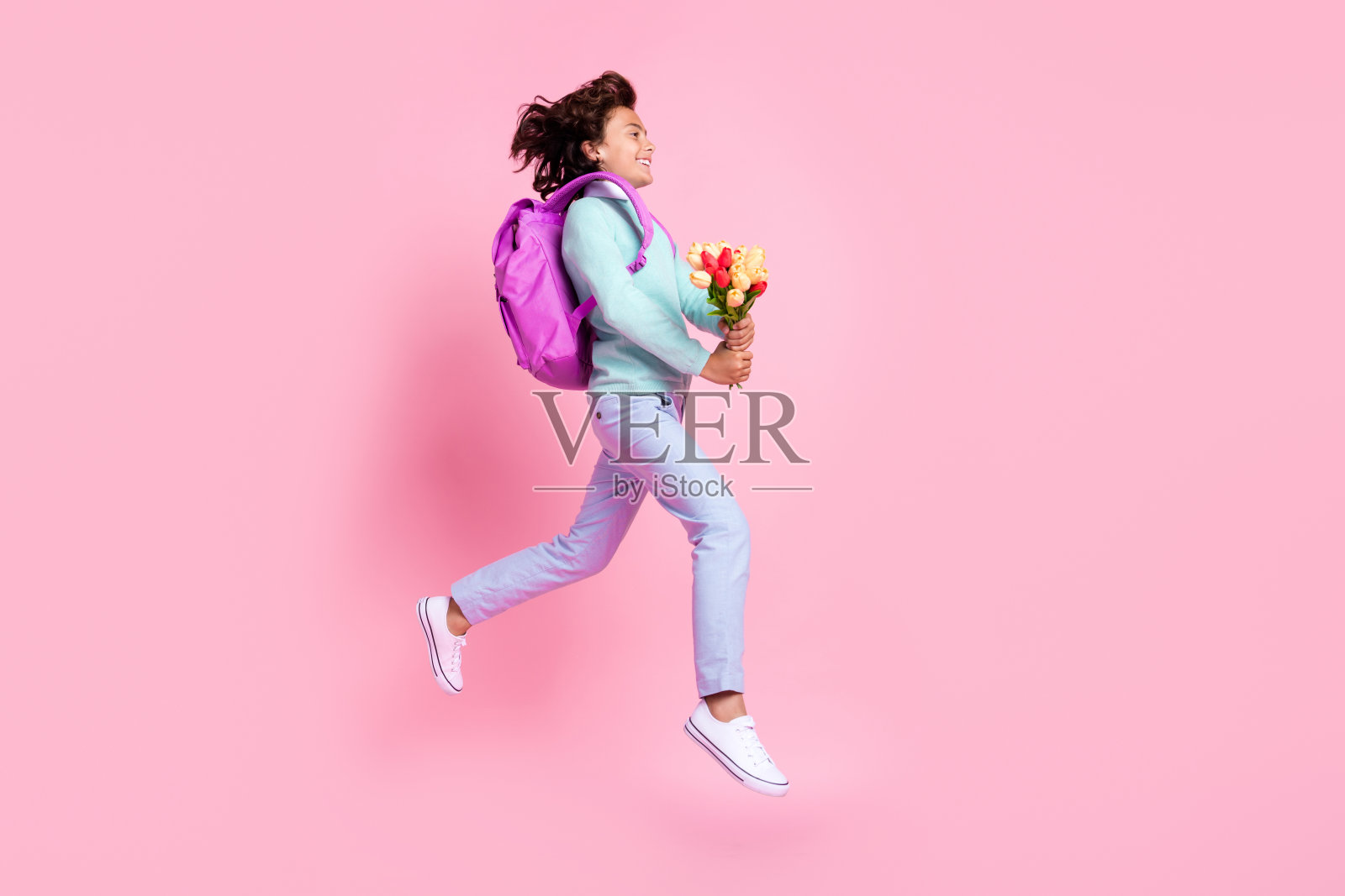 高兴的好男孩的侧面照片跳抱郁金香跑穿包蓝绿色衬衫裤子运动鞋孤立的粉红色背景照片摄影图片
