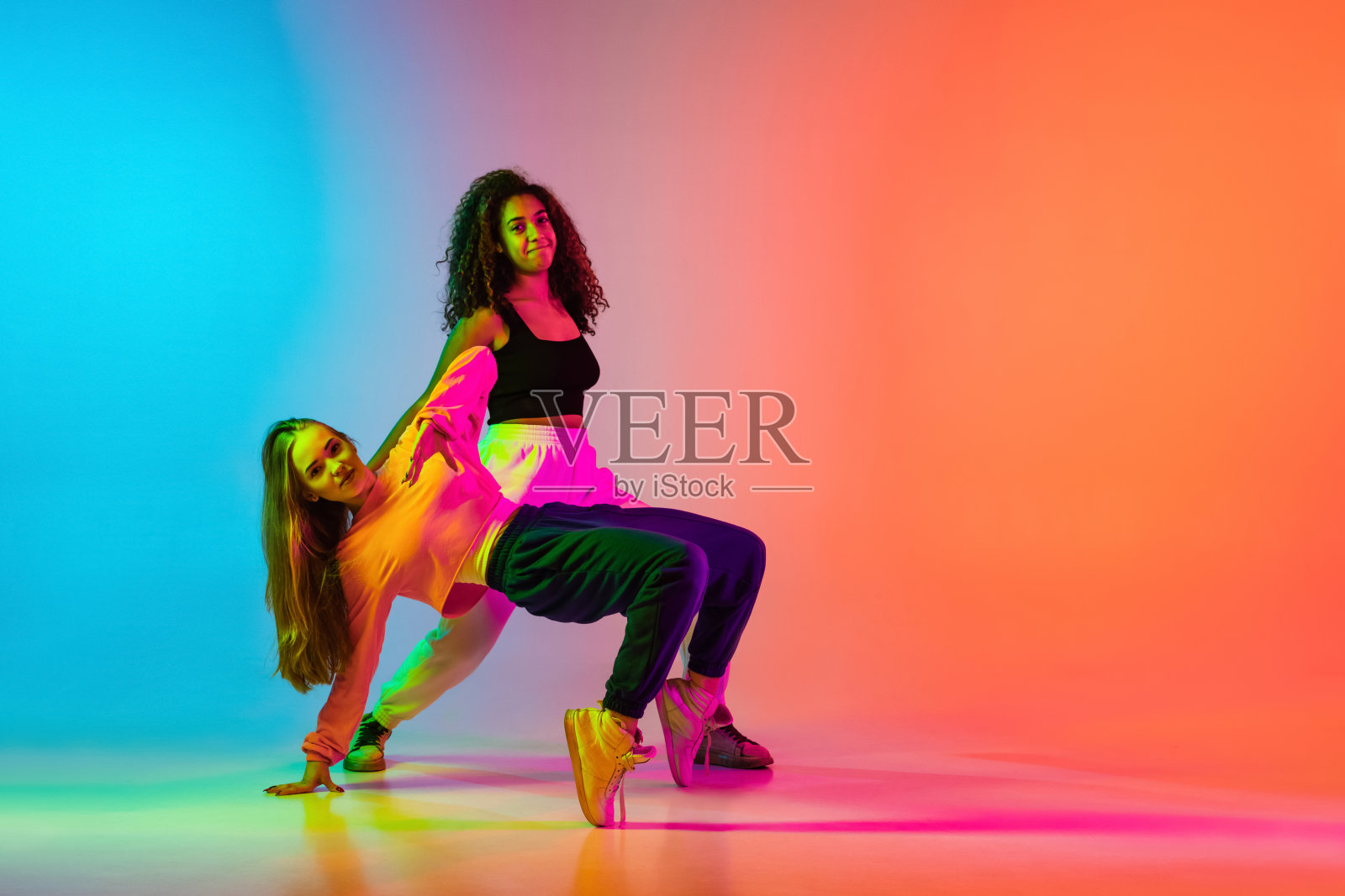 两个时髦的现代女孩在霓虹灯的渐变蓝橙色背景上跳嘻哈舞照片摄影图片