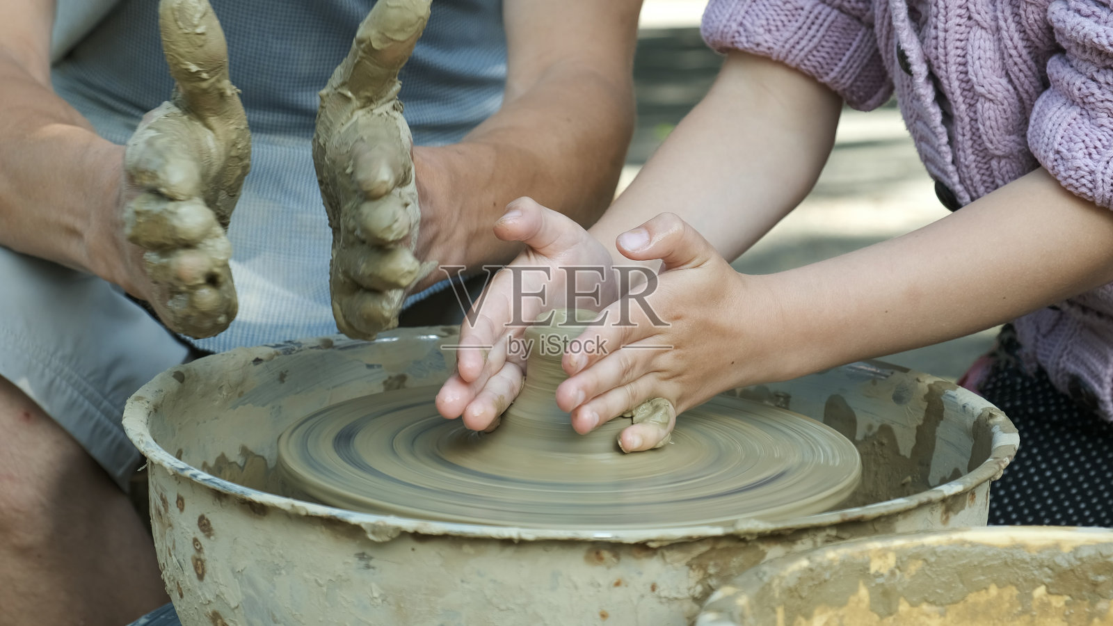 陶艺大师教孩子用电动的现代陶艺轮制作陶罐。一个孩子和一个成年人的手都沾满了泥土。教学陶器照片摄影图片