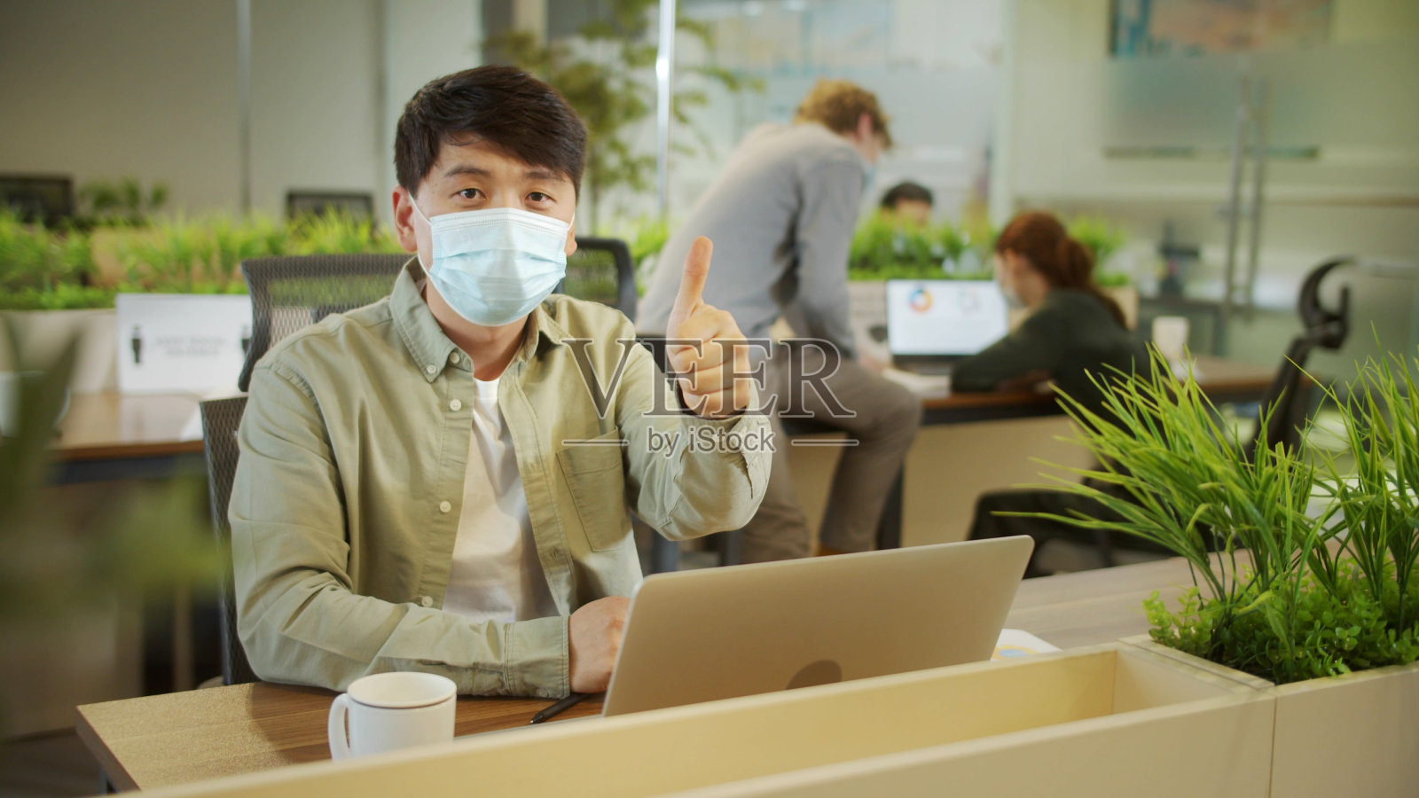 一位年轻的同事戴着口罩坐在那里给双手消毒照片摄影图片