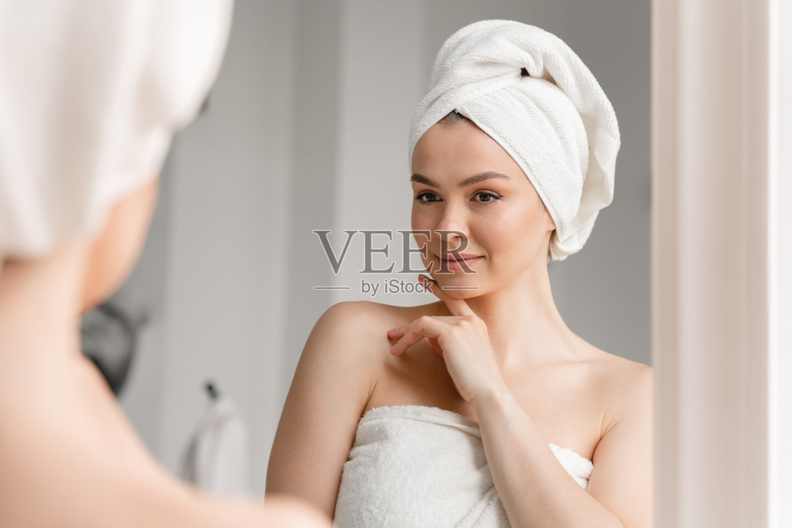 白种白种的女人用干净的年轻的干净的皮肤在spa浴巾看着镜子。美容、身体和头发护理。女孩在家洗完澡后淋浴照片摄影图片